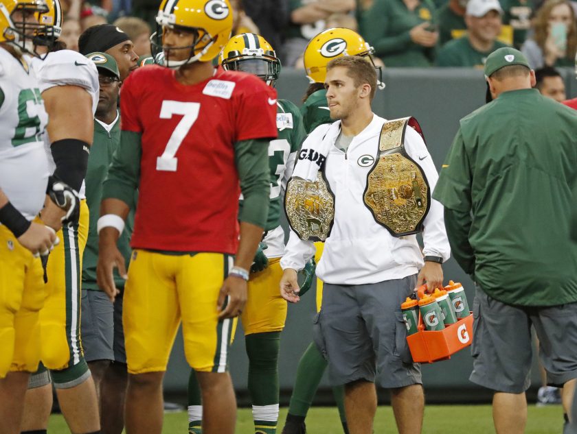 A Green Bay Packers waterboy carries water and wrestling belts.