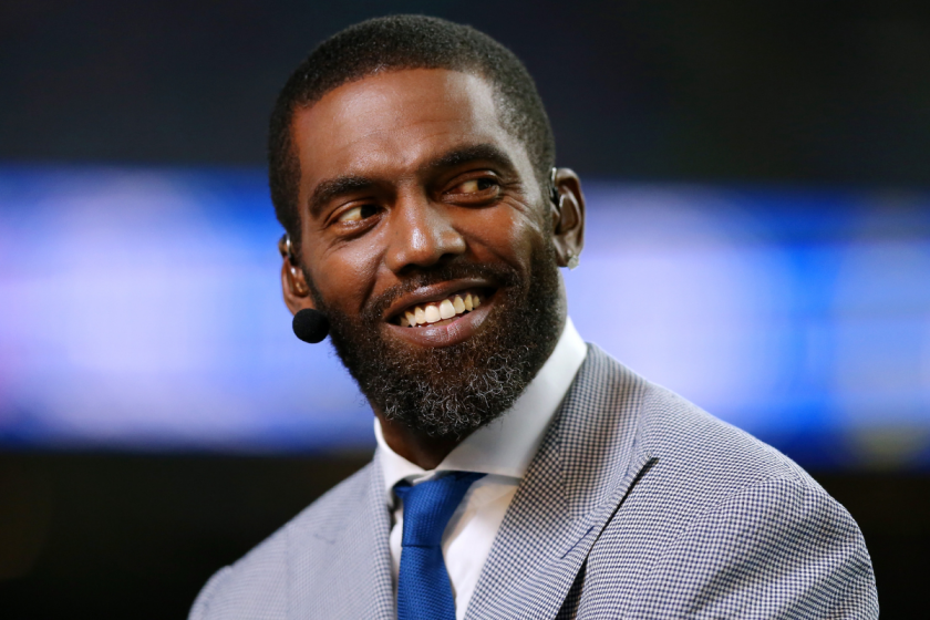 Randy Moss smiles while broadcasting an NFL game.