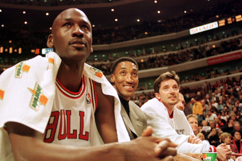 Michael Jordan sits on the bench next to two teammates. All are looking up