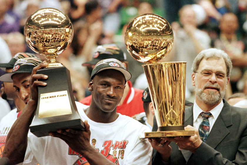 Michael Jordan and Phil Jackson raise trophies on the court. 