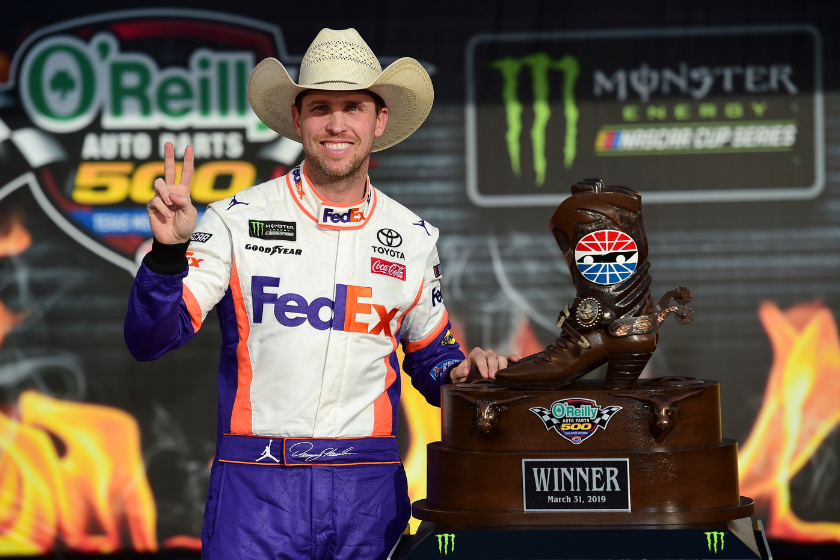 denny hamlin posing with cowboy shoes trophy at texas motor speedway