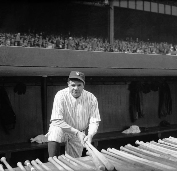 Babe Ruth holds a couple of baseball bats.