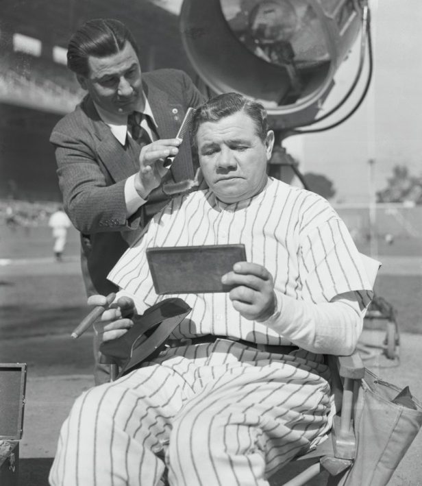 Babe Ruth gets his hair cut on field.