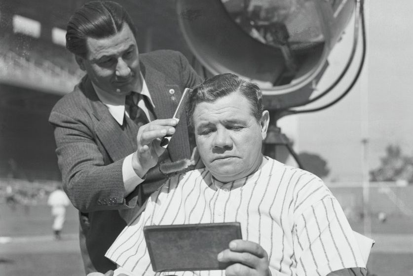 Babe Ruth gets his hair cut on field.