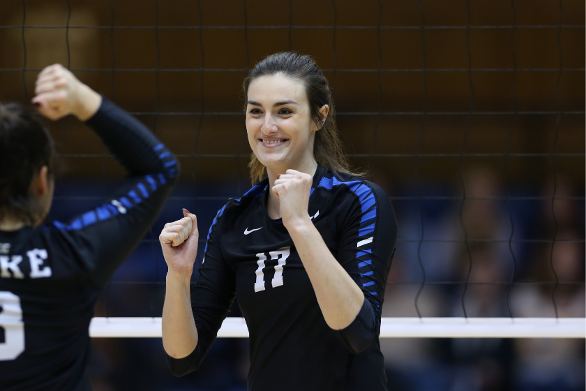 duke volleyball player samantha amos smiles with raised fists in front of a volleyball net