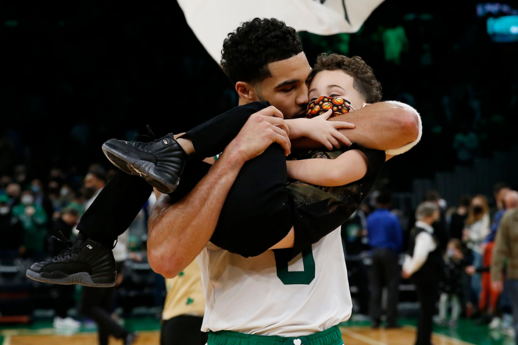 basketball player Jayson Tatum holds and kisses his son on the court after a game