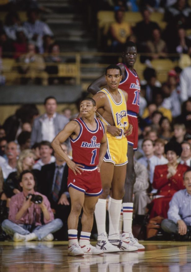 Muggsy Bogues stands next to two players during an NBA game.