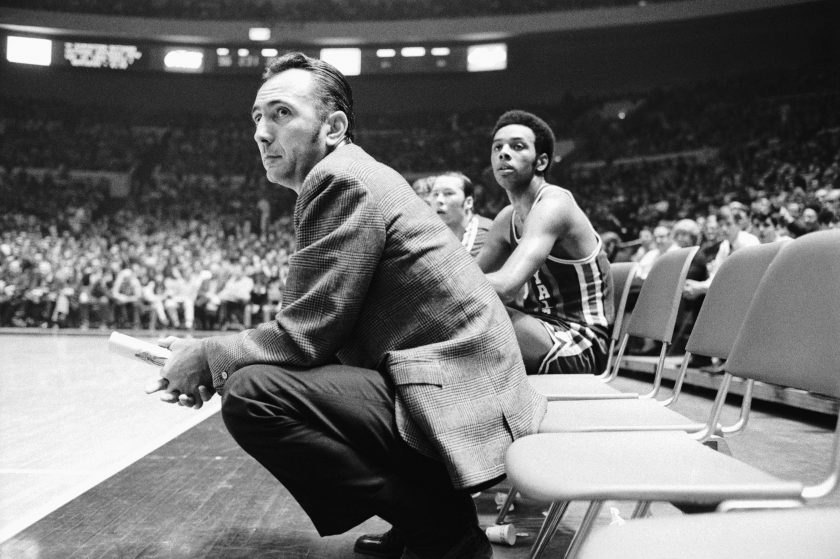 Bob Cousy squats on the court.