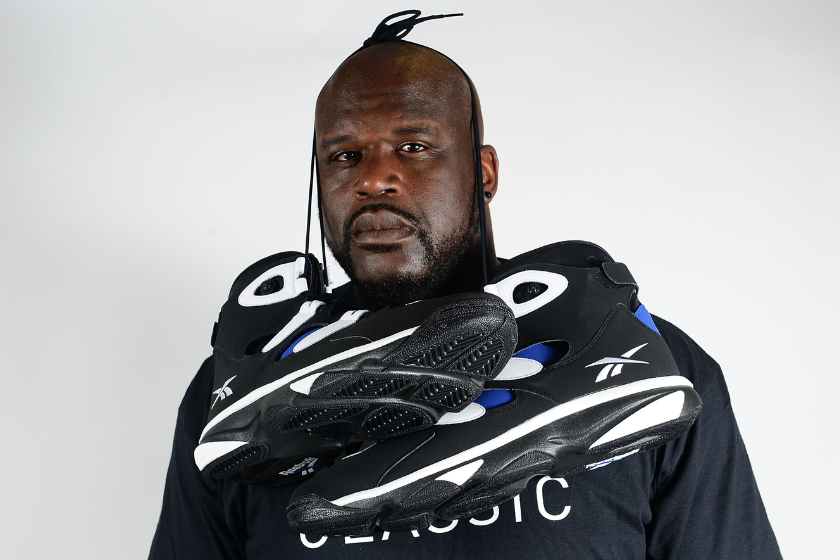 Former NBA basketball player Shaquille O'Neal poses with Reebok sneakers at the Reebok Classic Breakout at Philadelphia University, showcasing his massive shoe size. 