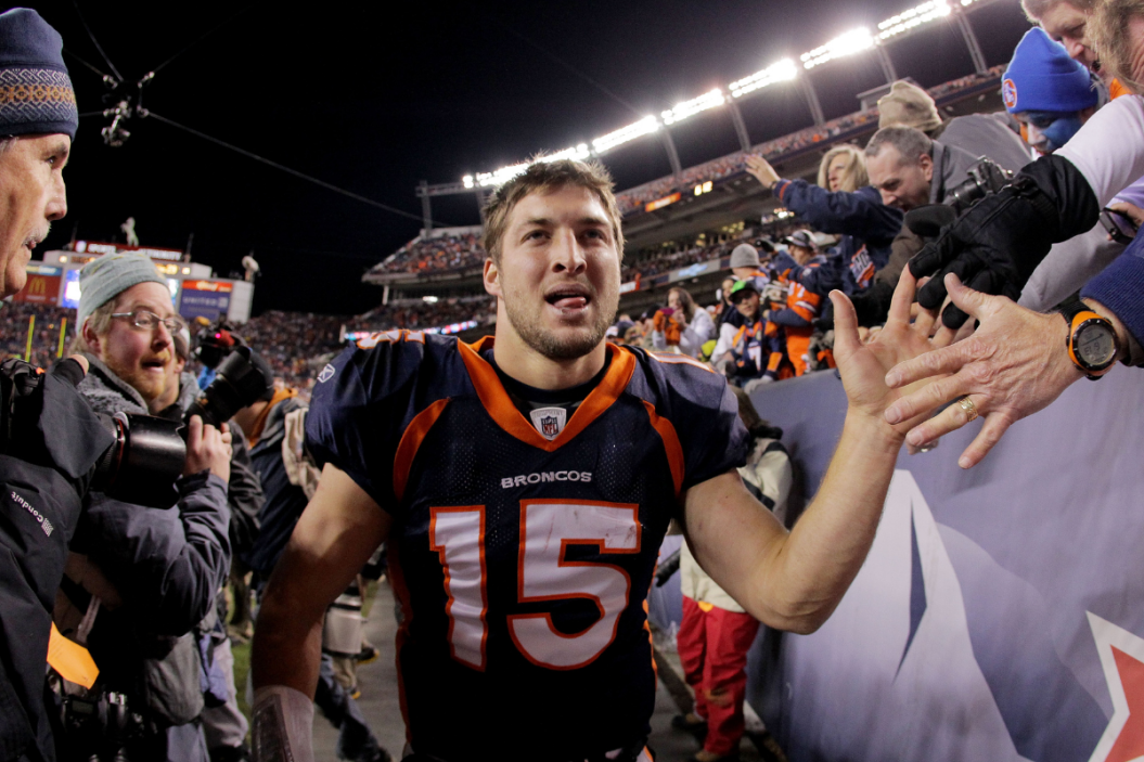 American football player Tim Tebow high-fives fans on the sidelines.