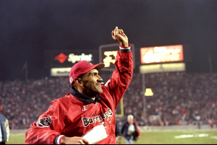 a man wearing a red hat and jacket raises his fist in victory on a football field
