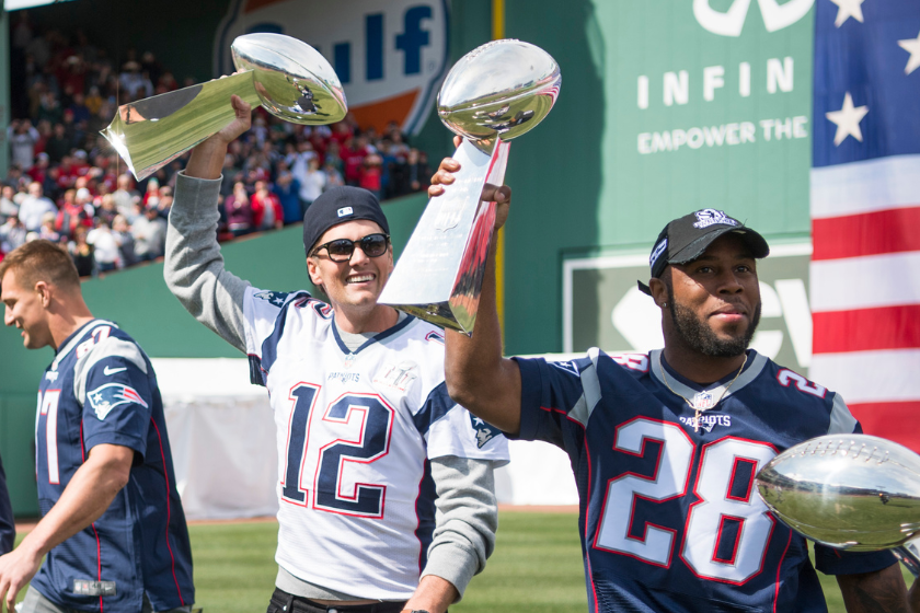 Tom Brady #12 and James White #28 of and the New England Patriots hold Lombardi trophies during a ceremony in recognition of their Super Bowl victory at Fenway Park