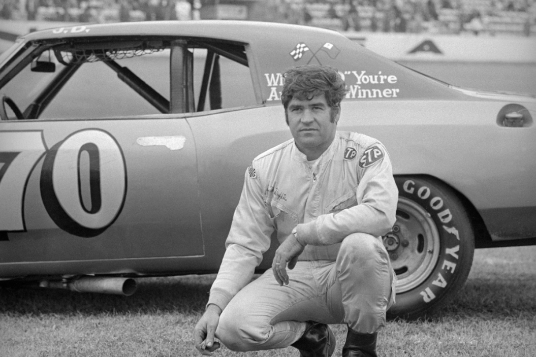J.D. McDuffie kneeling on the field in front of the rear of the car in 1973