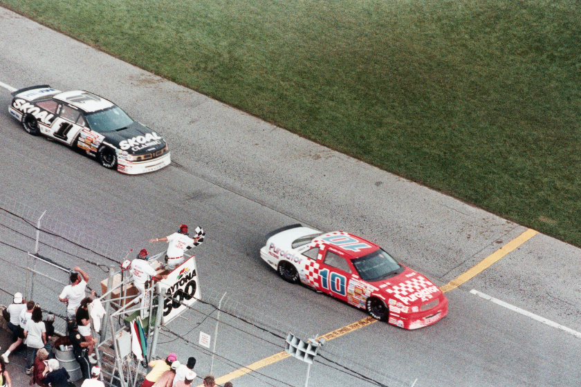 Les officiels de la course agitent le drapeau à damiers au-dessus de Derrike Cope, dans sa voiture 10 rouge et blanche, alors qu'il remporte le Daytona 500 1990