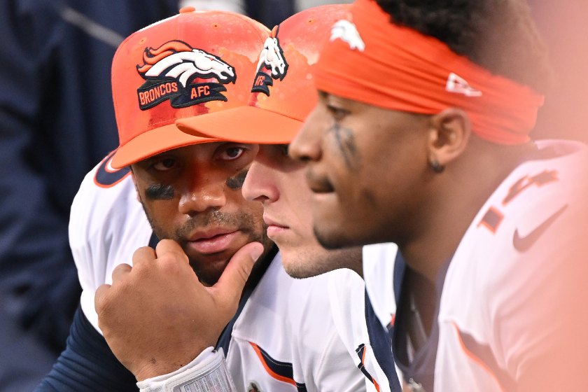 Russell Wilson #3 of the Denver Broncos confers with teammates on the sideline during their game against the Carolina Panthers at Bank of America Stadium