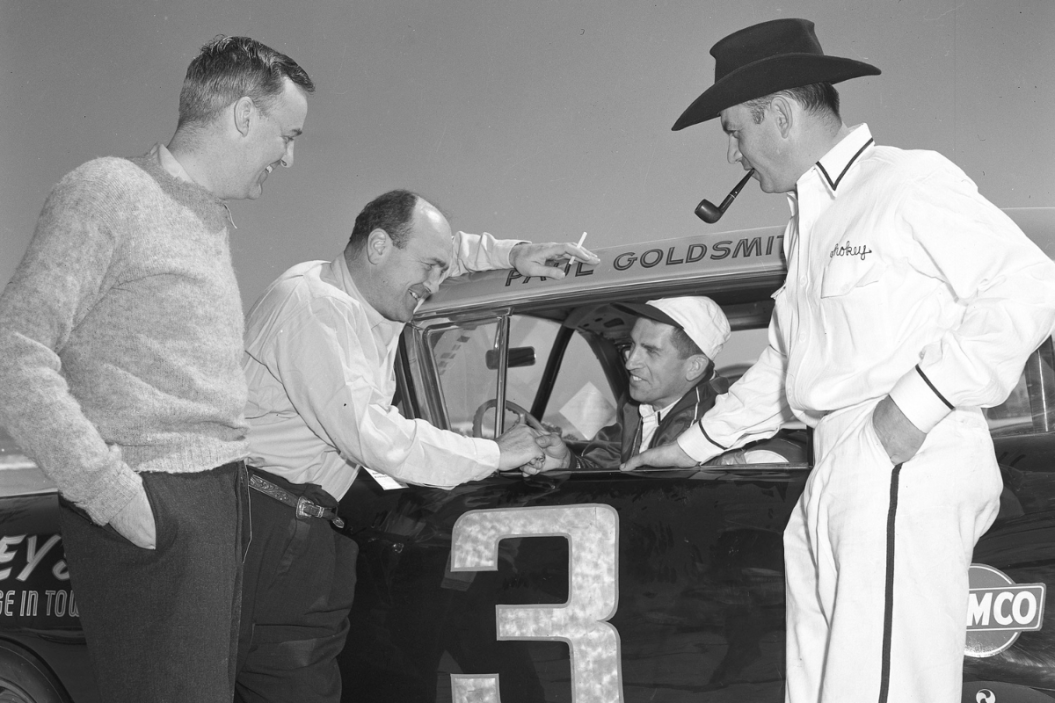 Driver Paul Goldsmith (in car) and car owner Henry “Smokey” Yunick (R) chat with a pair of unidentified men during Speed Weeks at the Daytona Beach-Road Course in 1958
