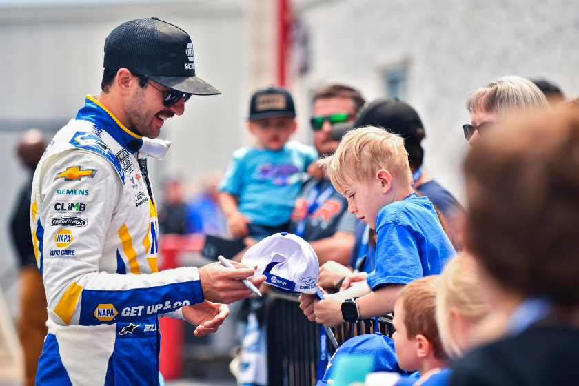 Chase Elliott signs an autograph for a young fan before the 2023 GEICO 500 at Talladega Superspeedway