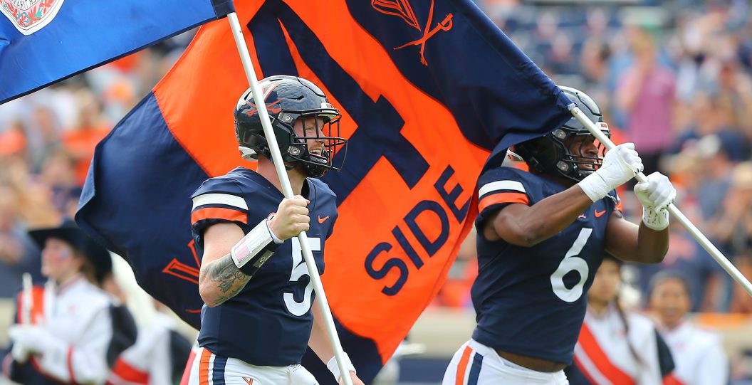 Virginia Cavaliers football players wave flags while walking into the field.