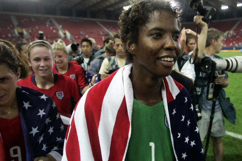 BRiana Scurry celebrates at the 2004 Olympics with a flag around her.