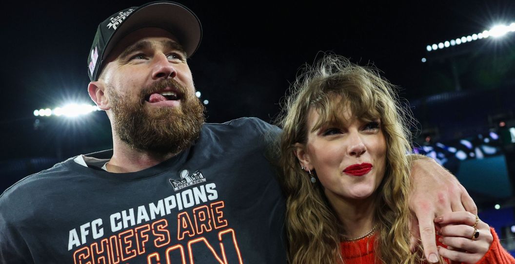 Travis Kelce holds his arm around Taylor Swift on field.