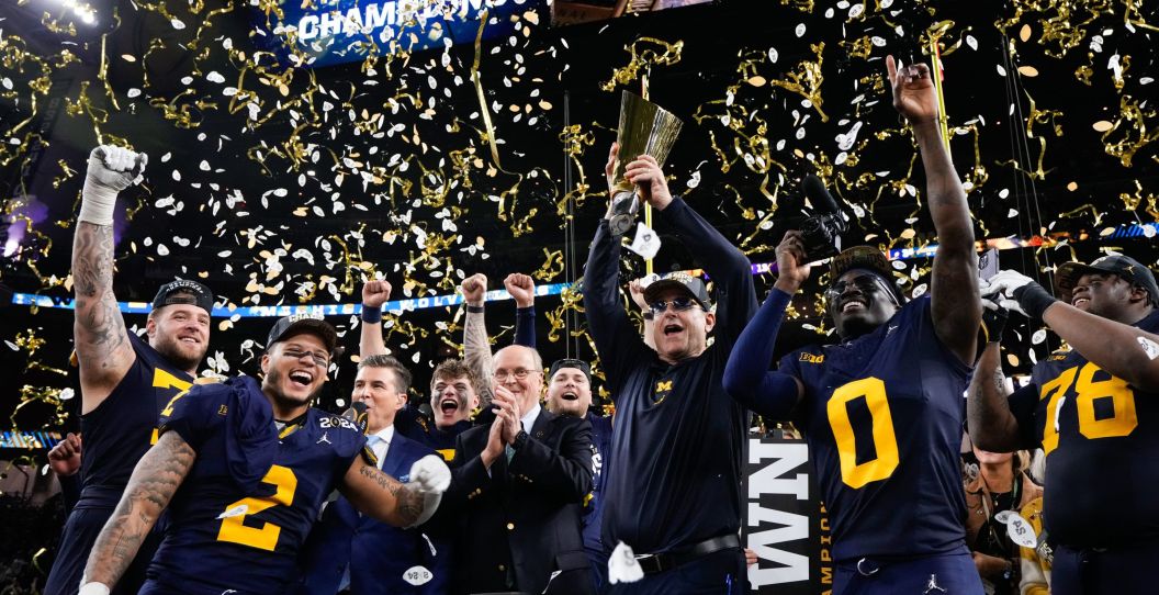 Michigan football celebrates the national title by holding up the trophy.