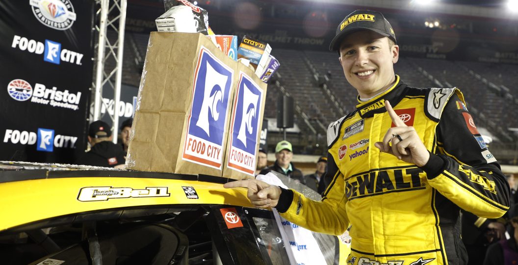 BRISTOL, TENNESSEE - APRIL 09: Christopher Bell, driver of the #20 DeWalt Power Stack Toyota, poses next to his winner sticker in victory lane after winning the NASCAR Cup Series Food City Dirt Race at Bristol Motor Speedway on April 09, 2023 in Bristol, Tennessee.