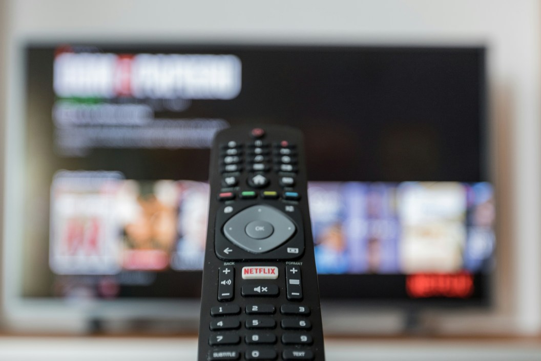 Black remote control on brown wooden table with blurred TV in the background